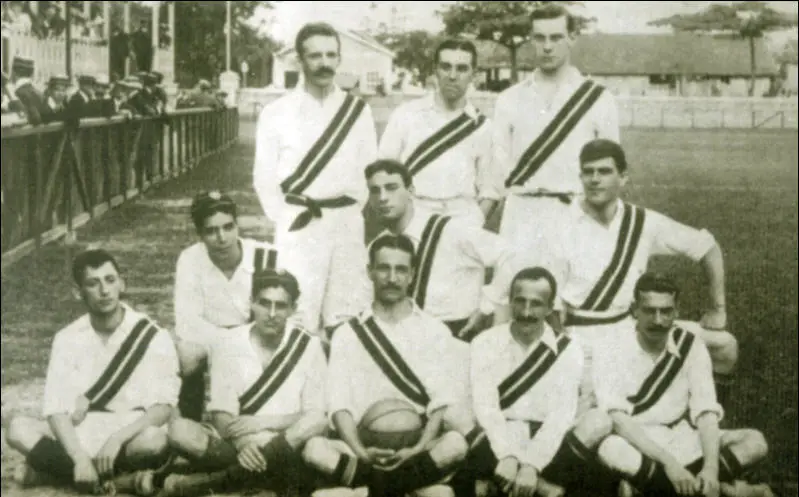 Grupo de homens em uniforme de futebol em fileiras, olhando para a câmera.