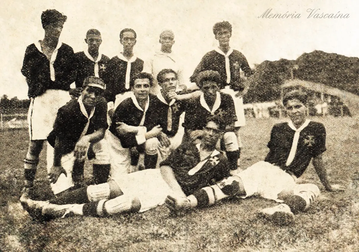 Grupo de futebolistas em uniforme, em preto e branco, em campo gramado.