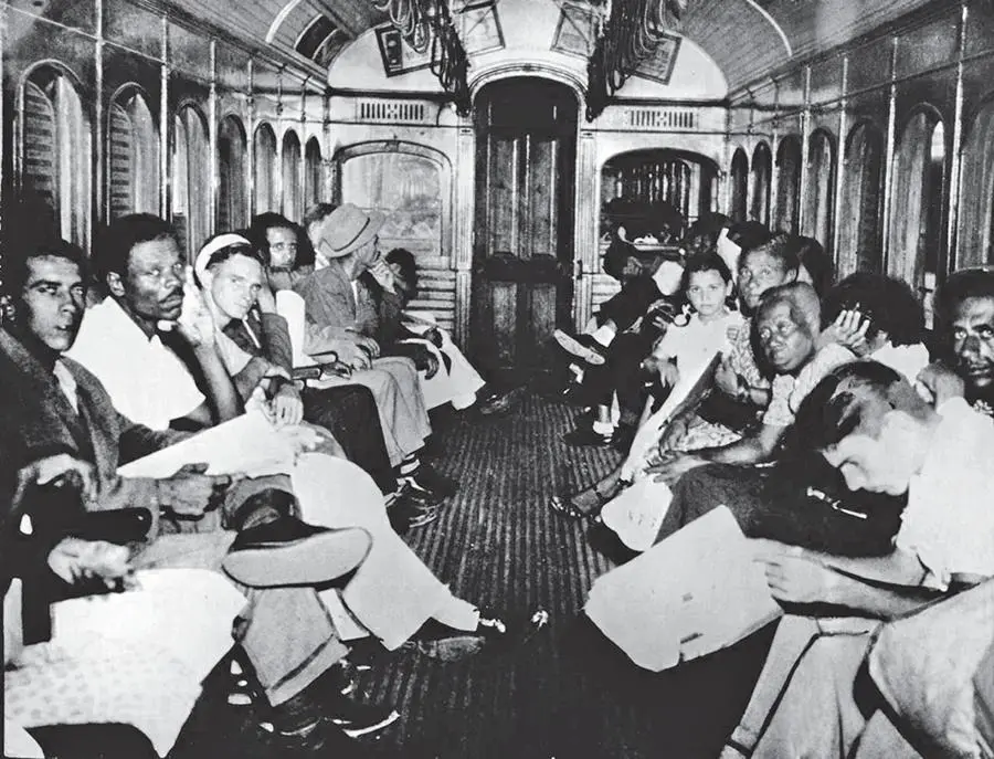 Interior de trem preto e branco com pessoas ocupadas.