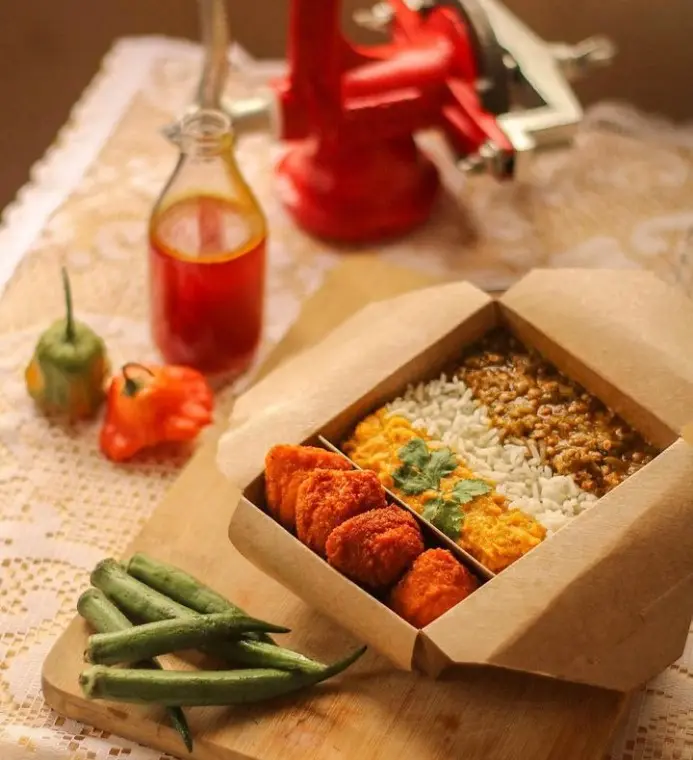 Almoço em caixa de papelão com pimentões, feijões verdes e pratos de arroz e lentilhas.