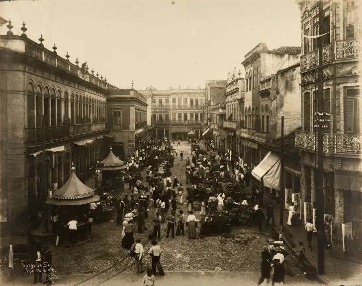Praça movimentada com construções antigas e pessoas caminhando.