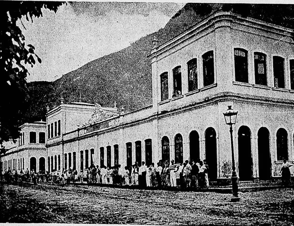 Grupo de pessoas em frente a edifício histórico, montanha ao fundo.