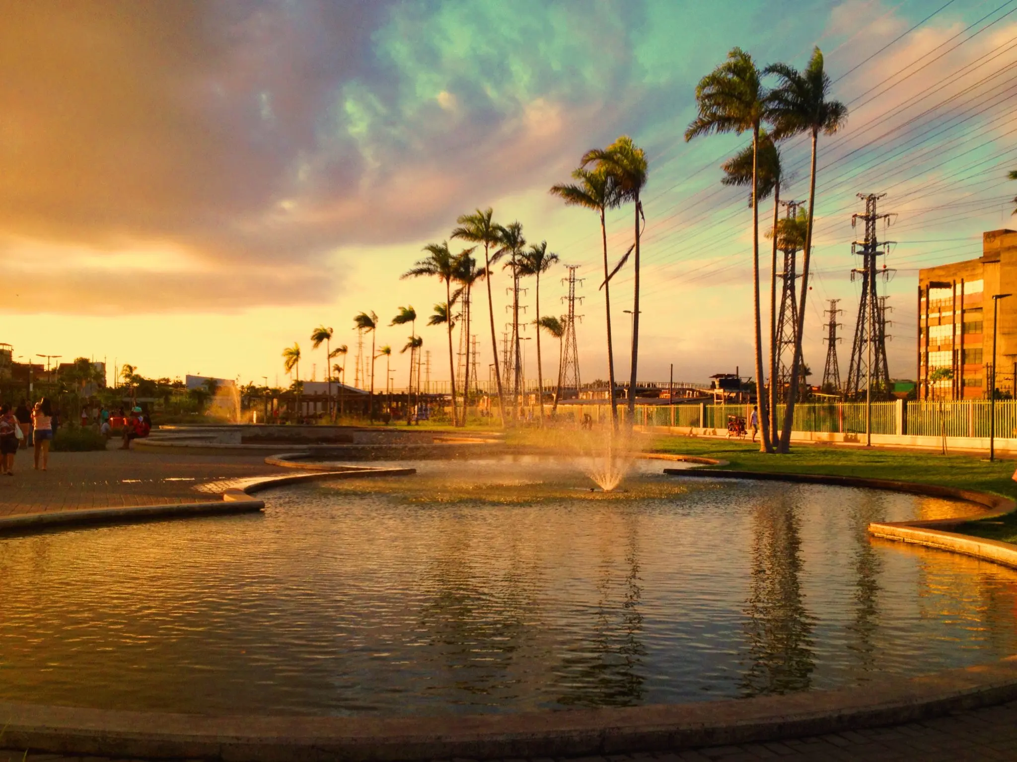 Parque ao pôr-do-sol com pessoas caminhando e árvores altas.