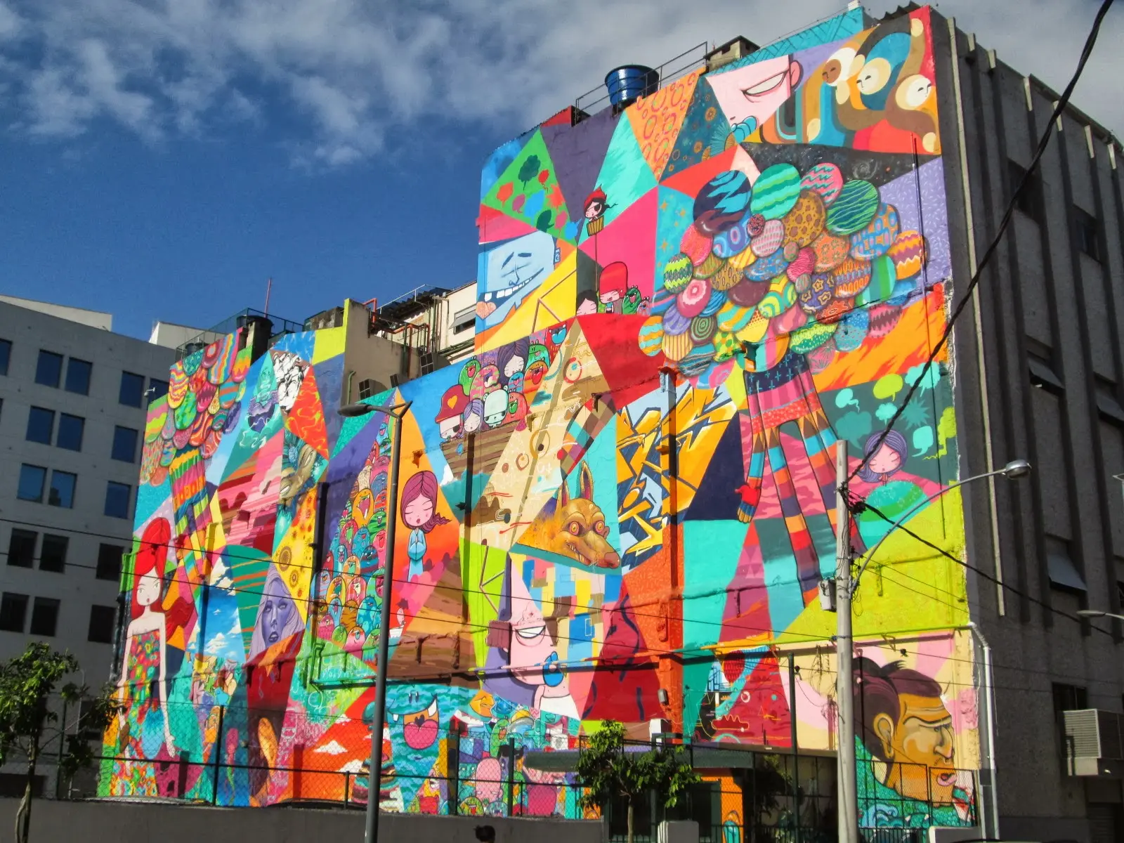 Graffiti colorido em parede de prédio, figuras geométricas e humanas vibrantes.