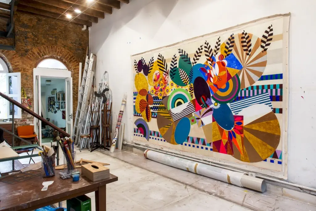 Ateliê com pintura abstrata, móveis e objetos artísticos.
