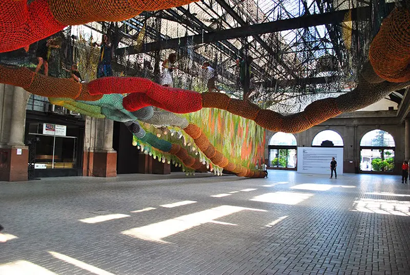 Espaço interno com instalação artística, escultura colorida e arcos de pedra.