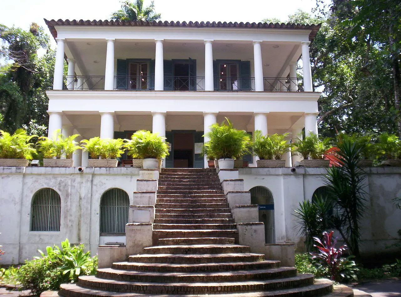 Solar colonial com varanda e janelas abertas, em ambiente tropical.