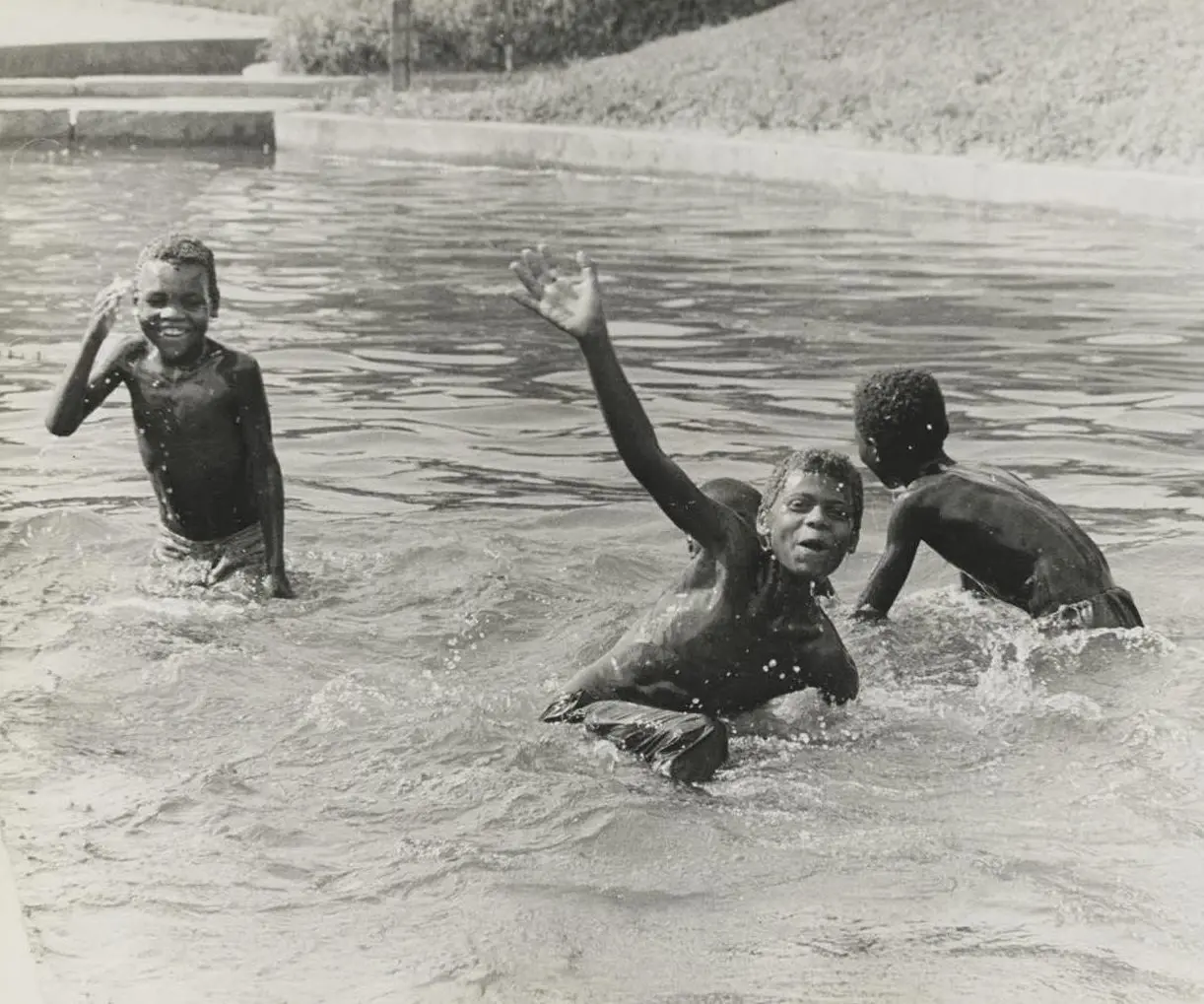 Três crianças brincando na água, sorrindo e mergulhando.