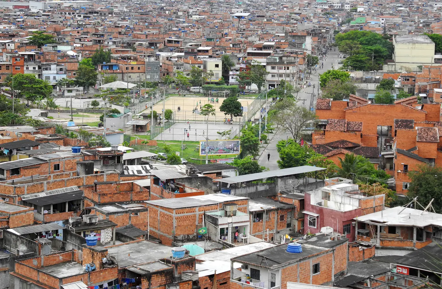 Área urbana com casas de tijolos vermelhos e campo de futebol.