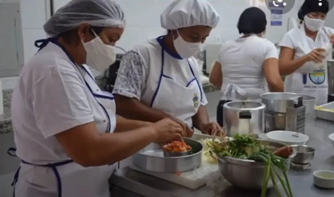 Cozinha industrial com pessoas organizando alimentos.