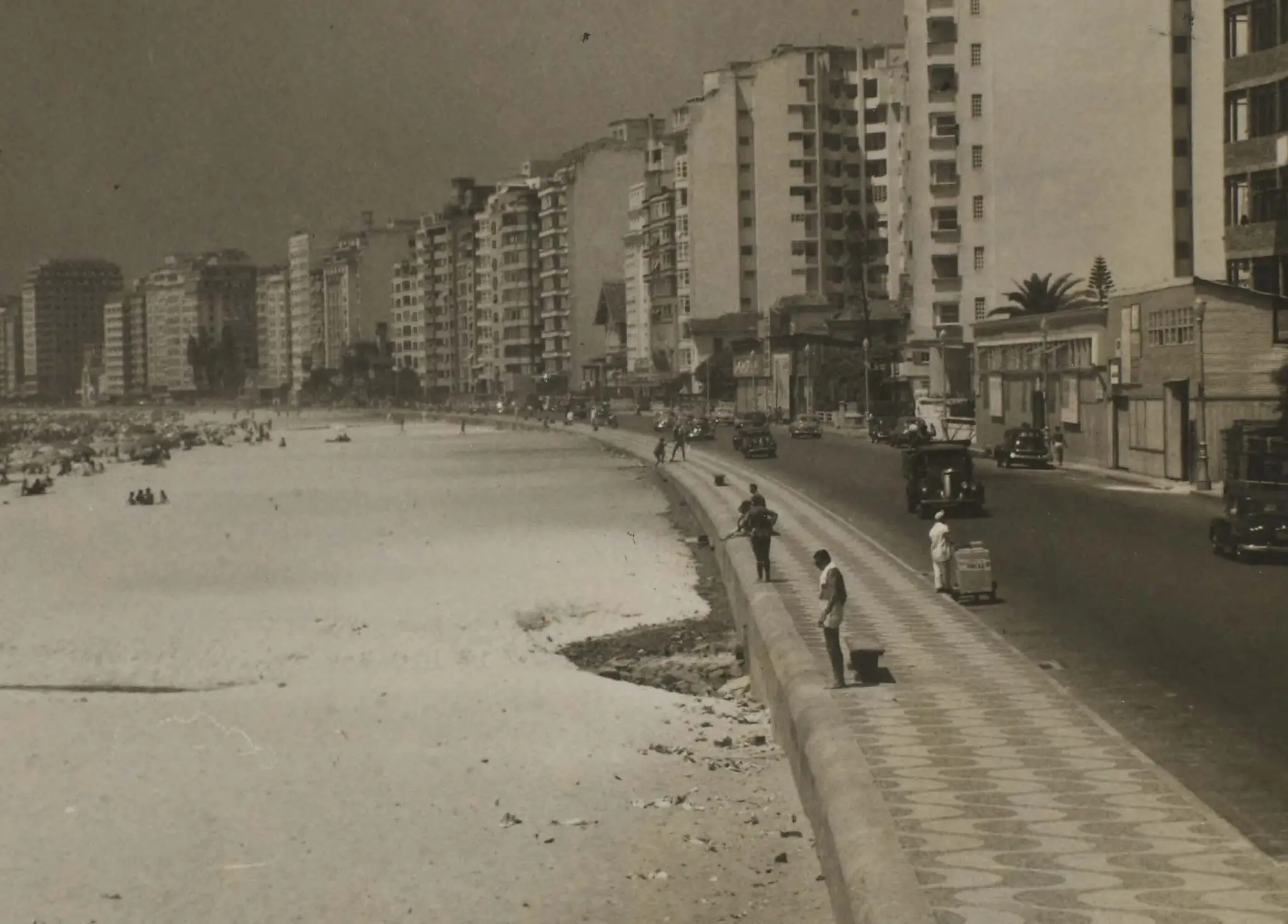Praia movimentada com edifícios urbanos ao fundo.