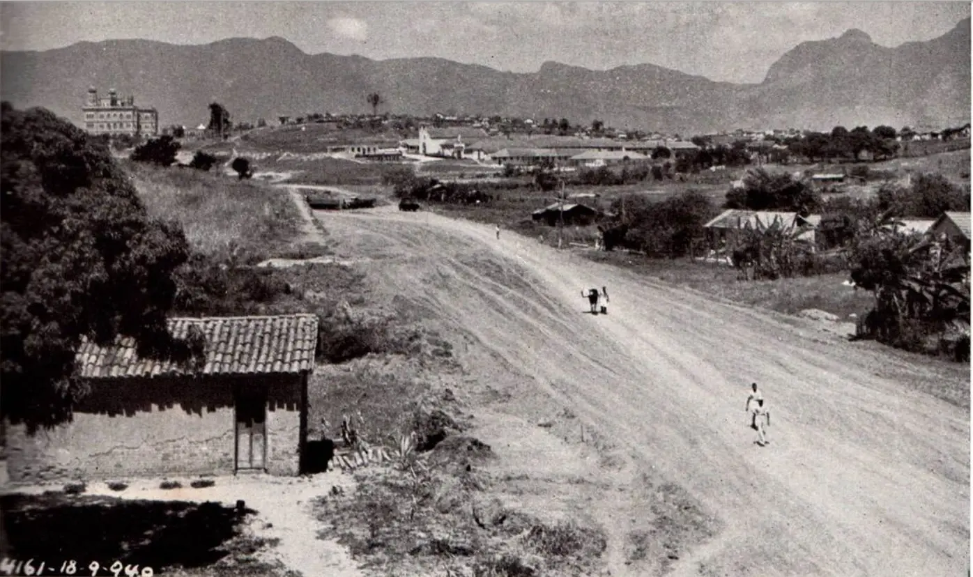 Avenida antiga com casarios à esquerda e área aberta à direita.
