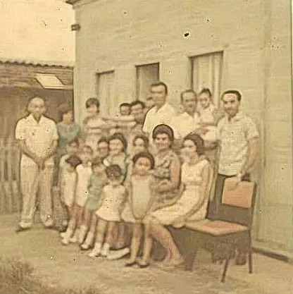 Família antiga em frente à casa, em tons de sepia.