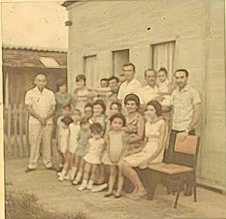 Família antiga em frente à casa simples, preto e branco.