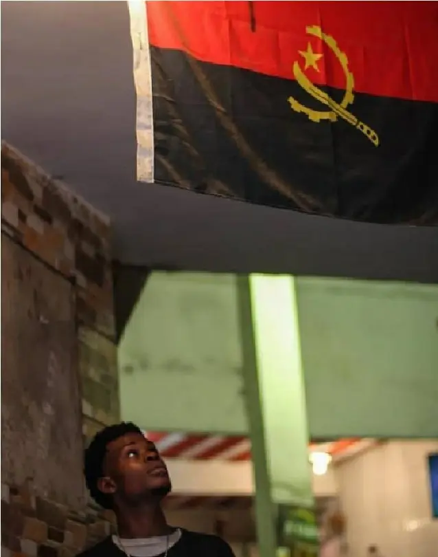 Homem olhando para cima com bandeira do Angola pendurada no teto.
