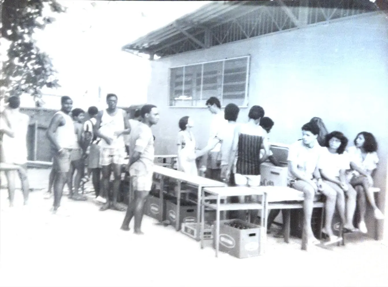 Grupo de pessoas reunidos em frente a prédio simples.