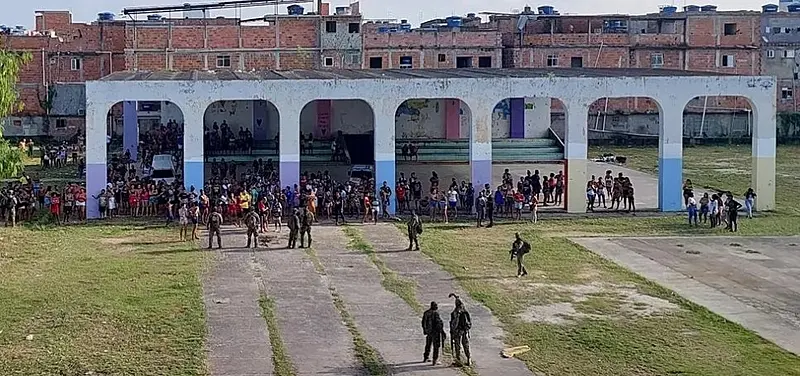 Arquibancadas e arcos coloridos em um local com multidões e construções ao fundo.