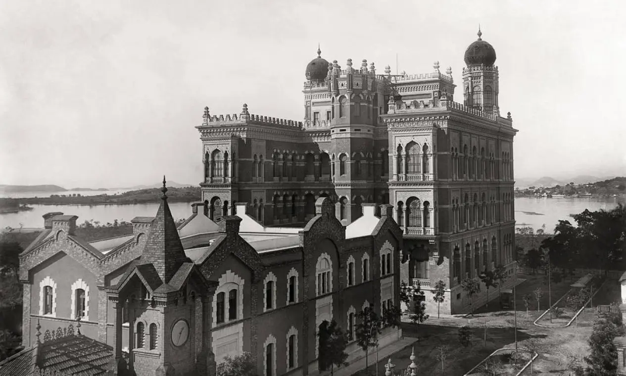 Edifício neogótico com torre inclinada e palácio com cúpulas.