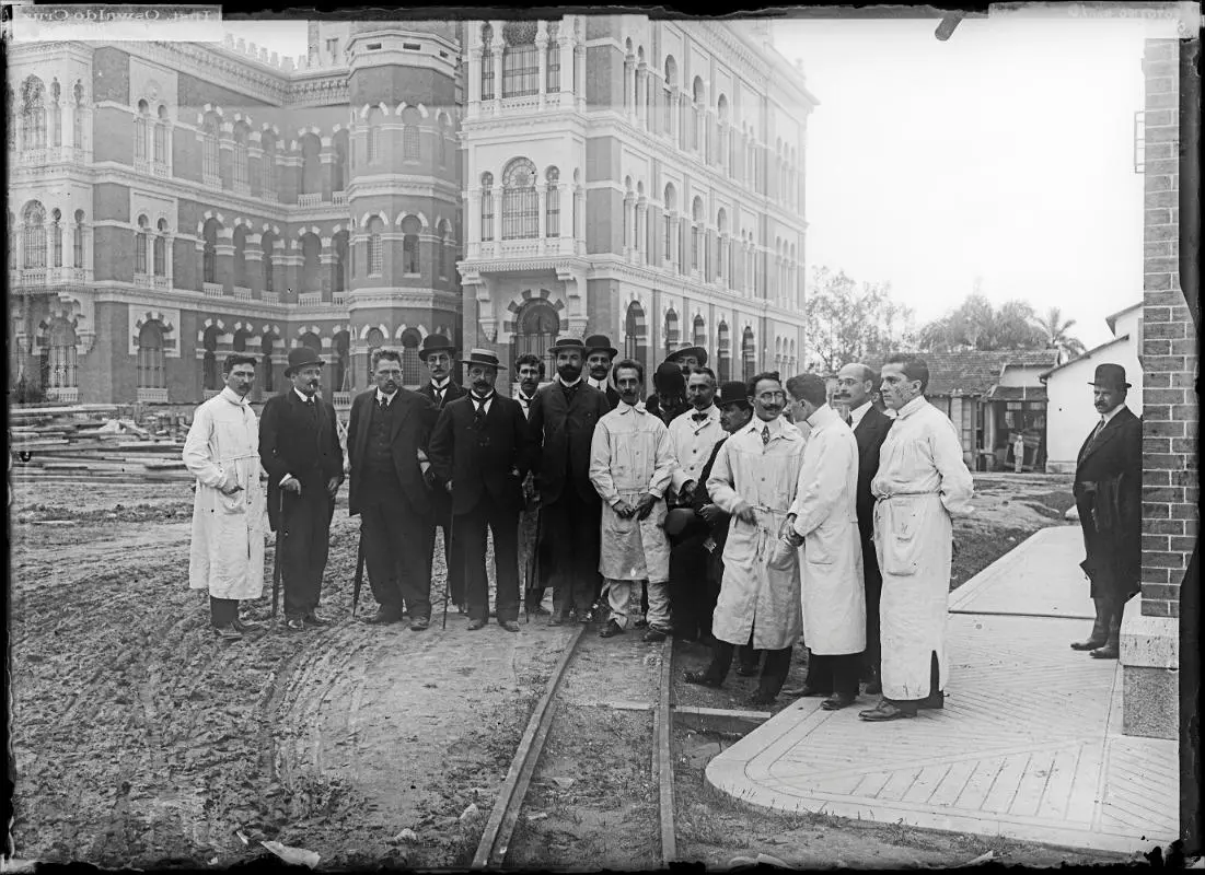 Imagem histórica em preto e branco de pessoas em frente a um edifício ornamental.
