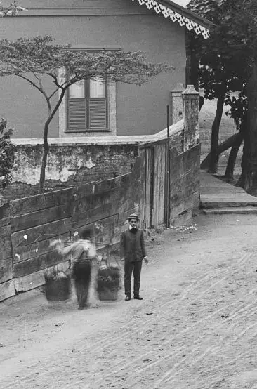 Criança caminhando pela rua segurando balde de água, roupas tradicionais.