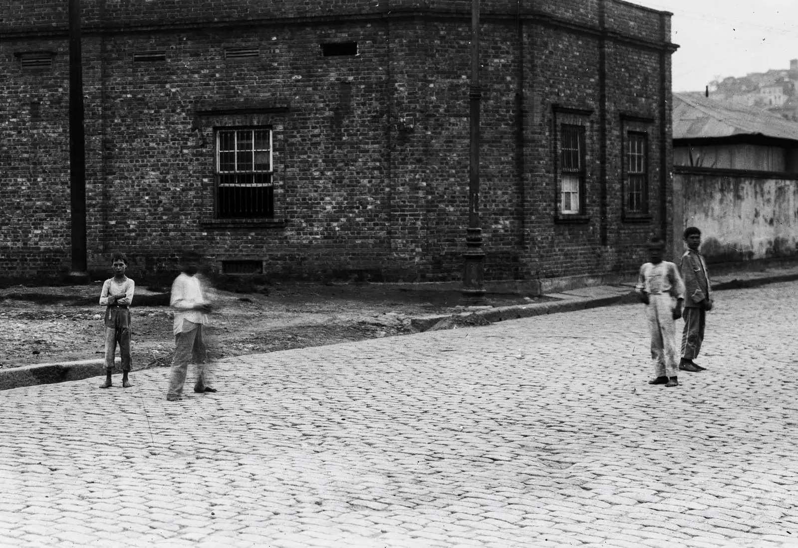 Rua coberta de pedras com prédio de tijolos e crianças.