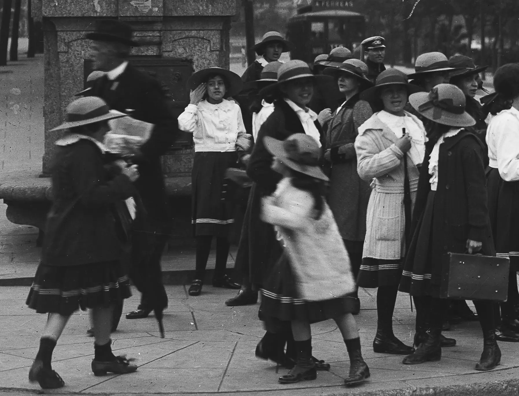 Crianças e adultos em ambiente urbano, uniformes escolares e elegantes do início do século XX.