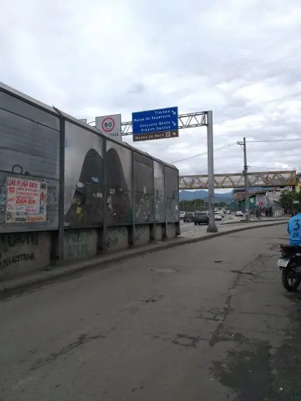 Via expressa com grafites coloridos, motos e carros distantes, sinal azul e ponte metálica.