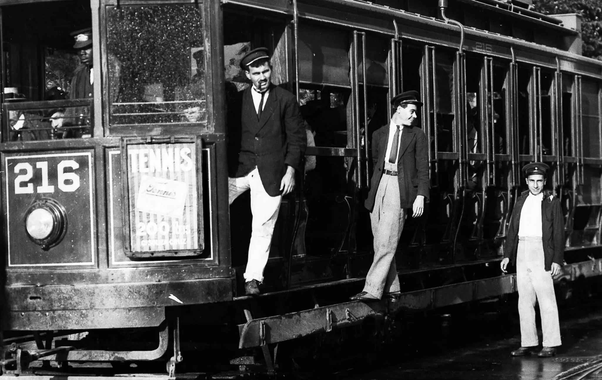 Fotografia preto e branco de um bonde com três homens saindo.