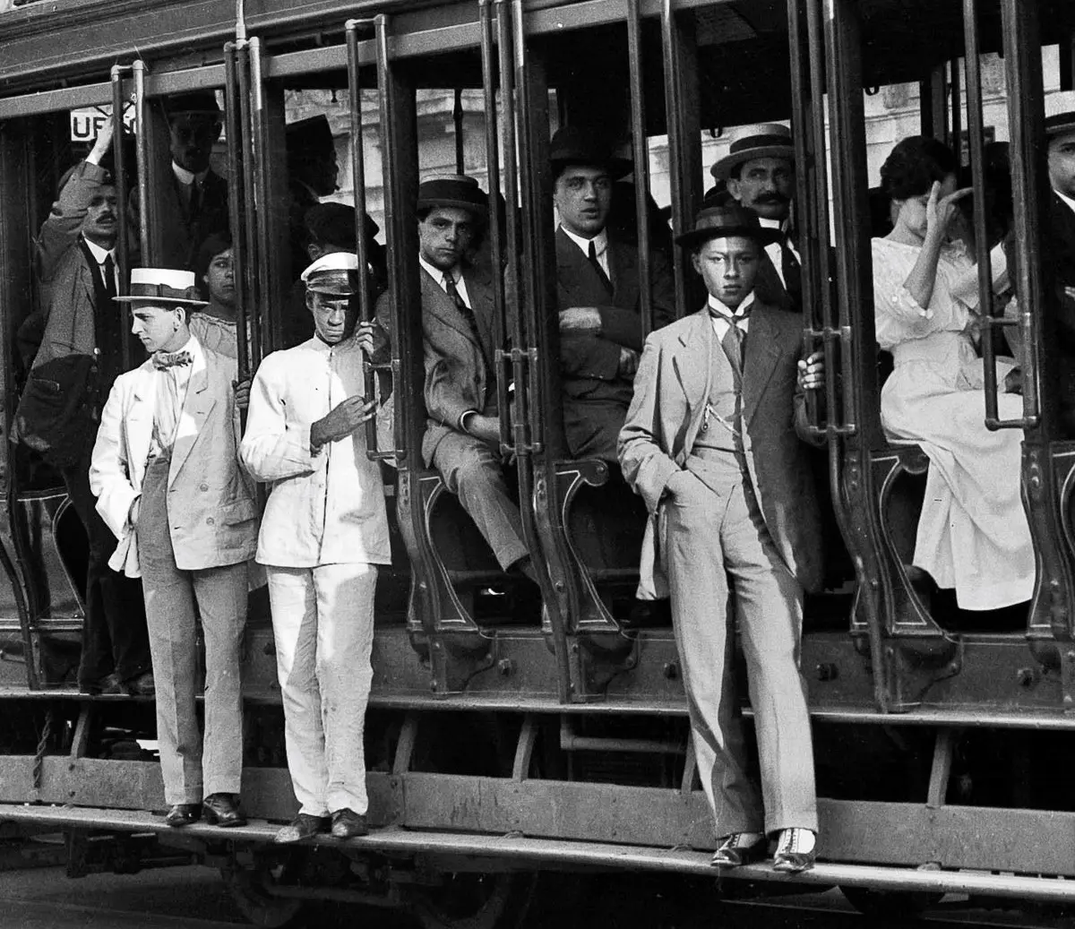 Pessoas em um trem, preto e branco, chapéus e ternos.