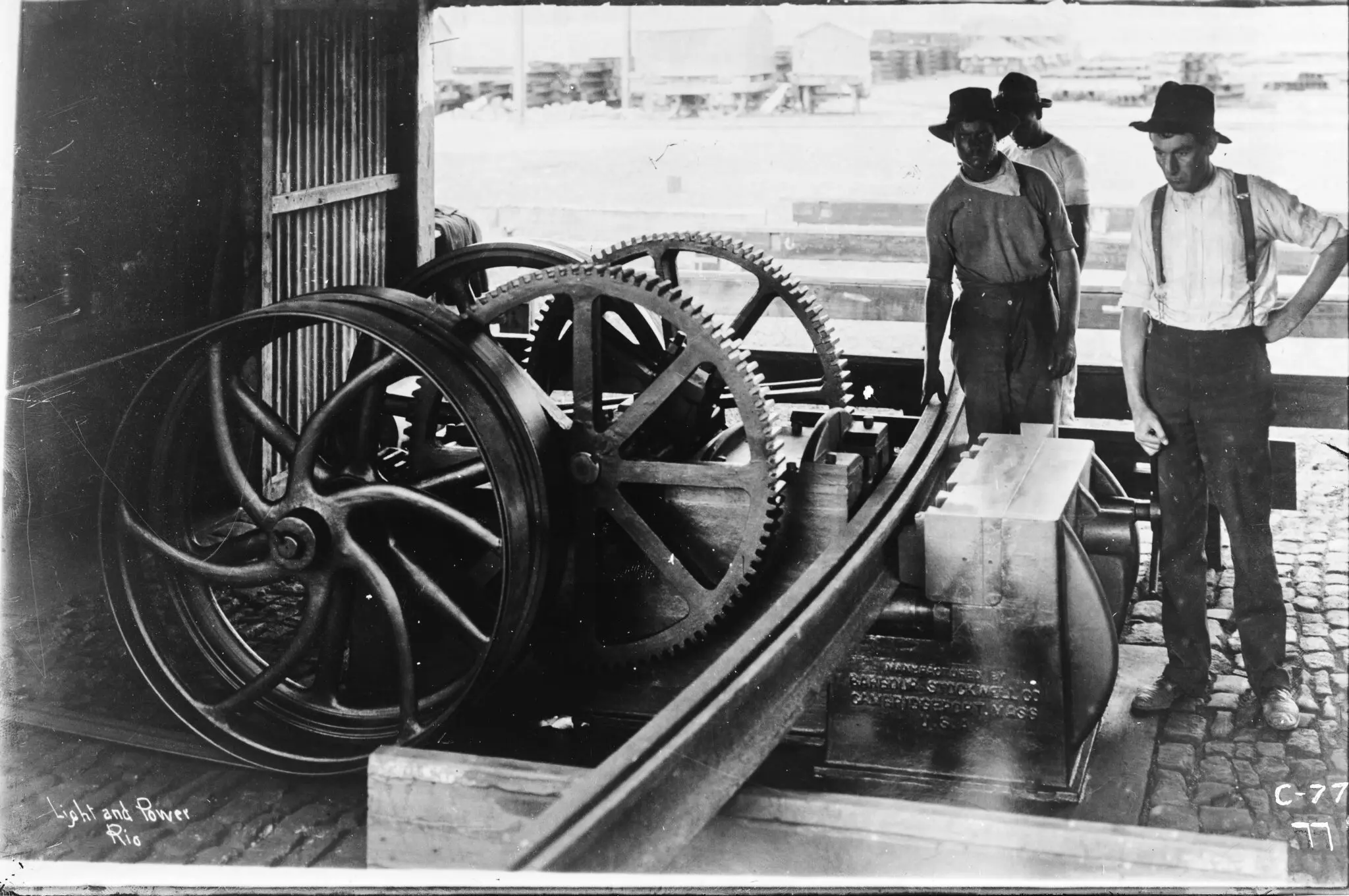 Três homens históricos perto de máquina industrial.