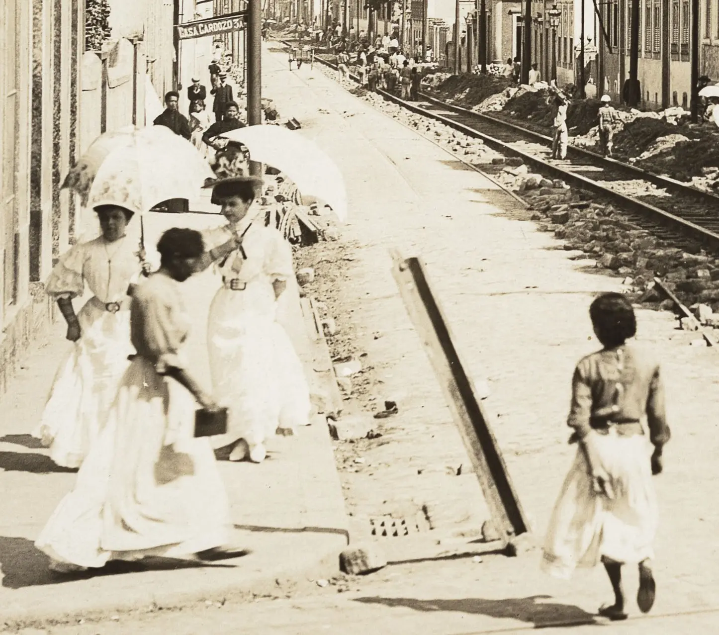Rua em construção com mulheres caminhando e criança sozinha.