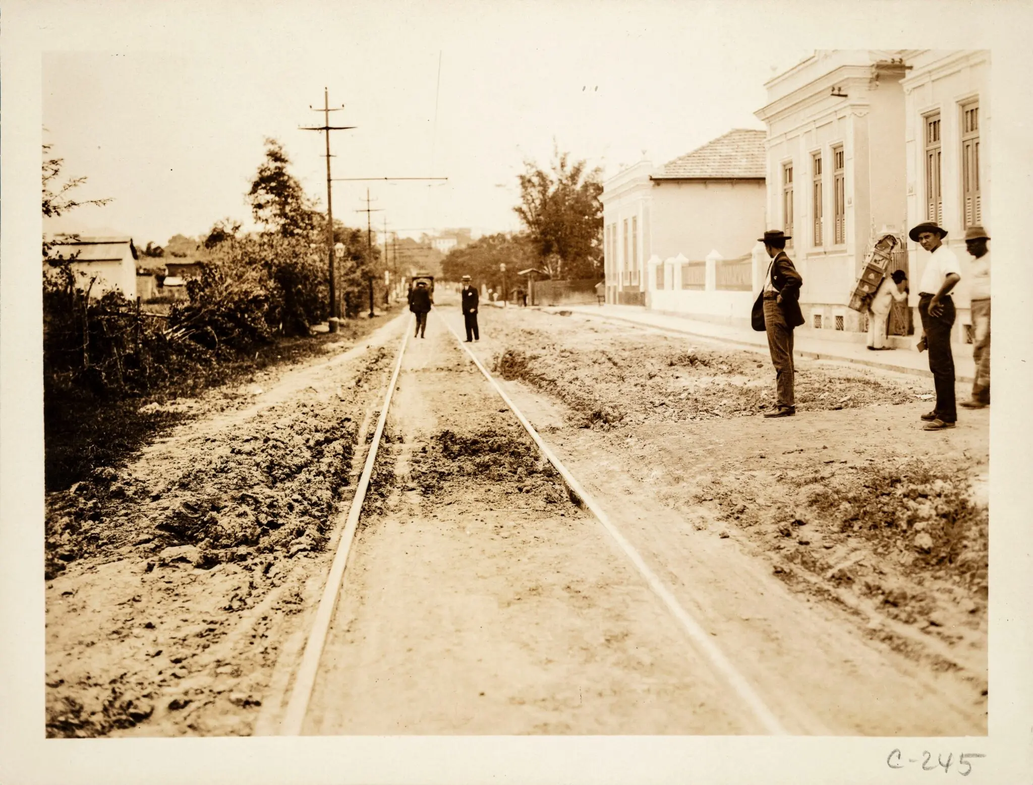 Rua antiga com trilhos e pessoas caminhando.
