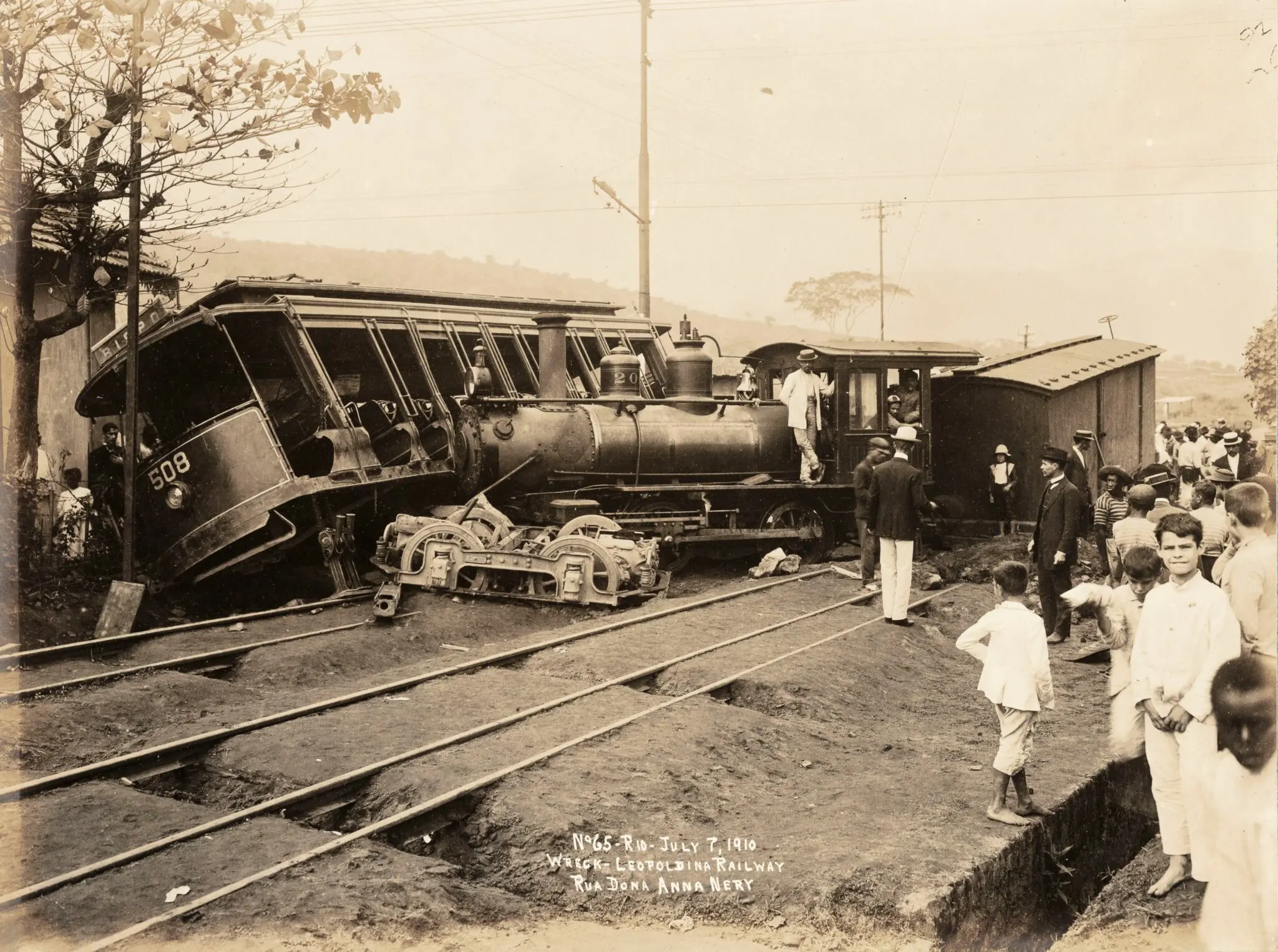 Acidente ferroviário em preto e branco, com locomotiva e vagão deslocados, pessoas observando.