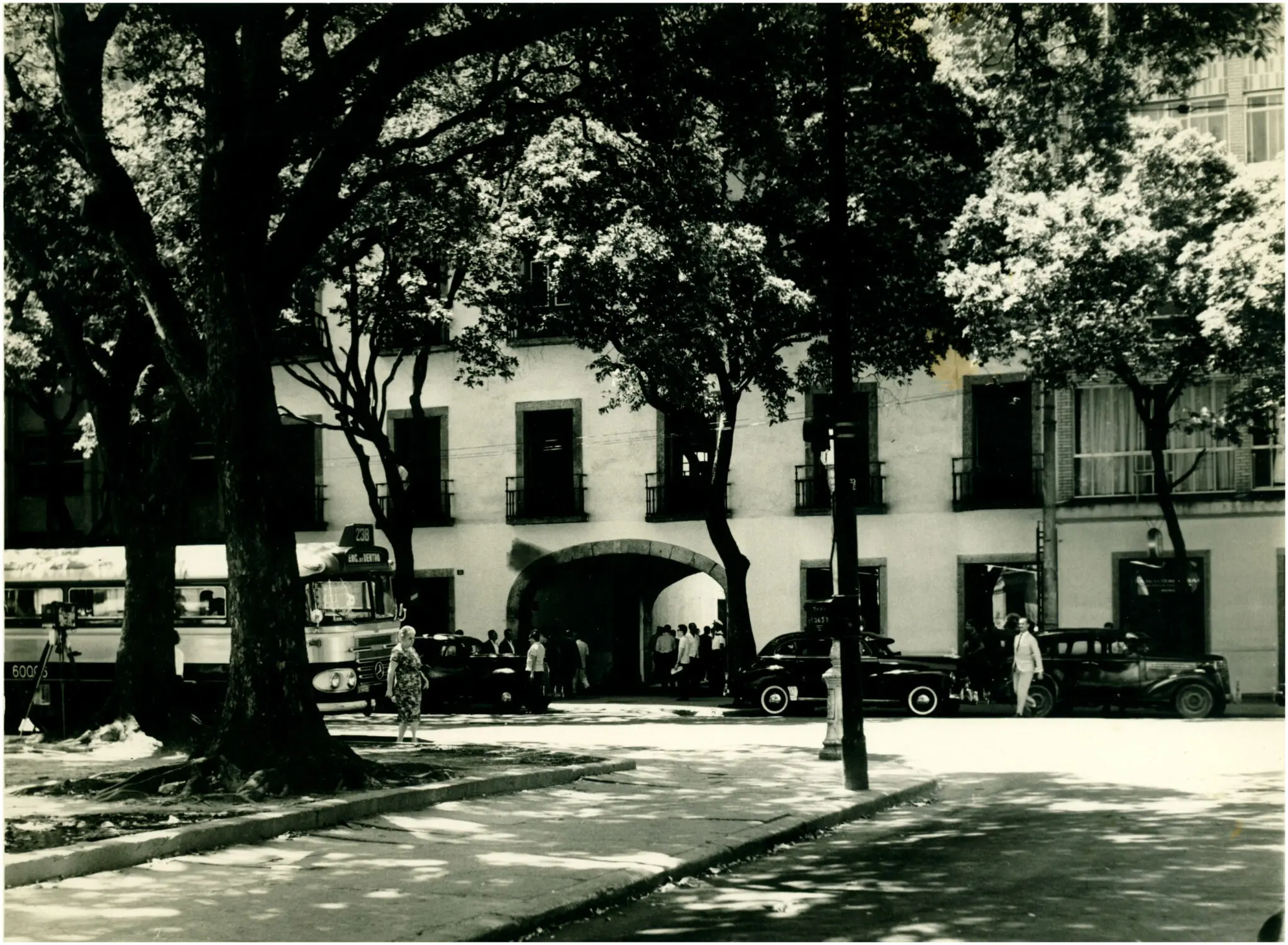 Arco histórico em preto e branco, com árvores e edifícios ao fundo.