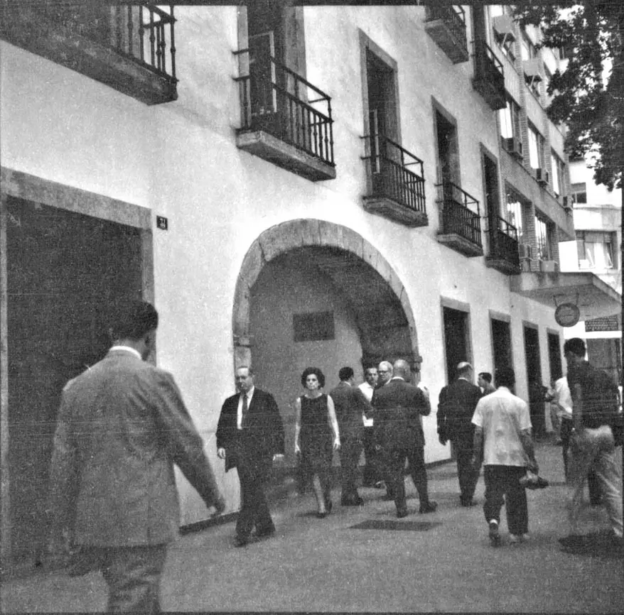 Grupo de pessoas em pátio, terno e arco com placa.