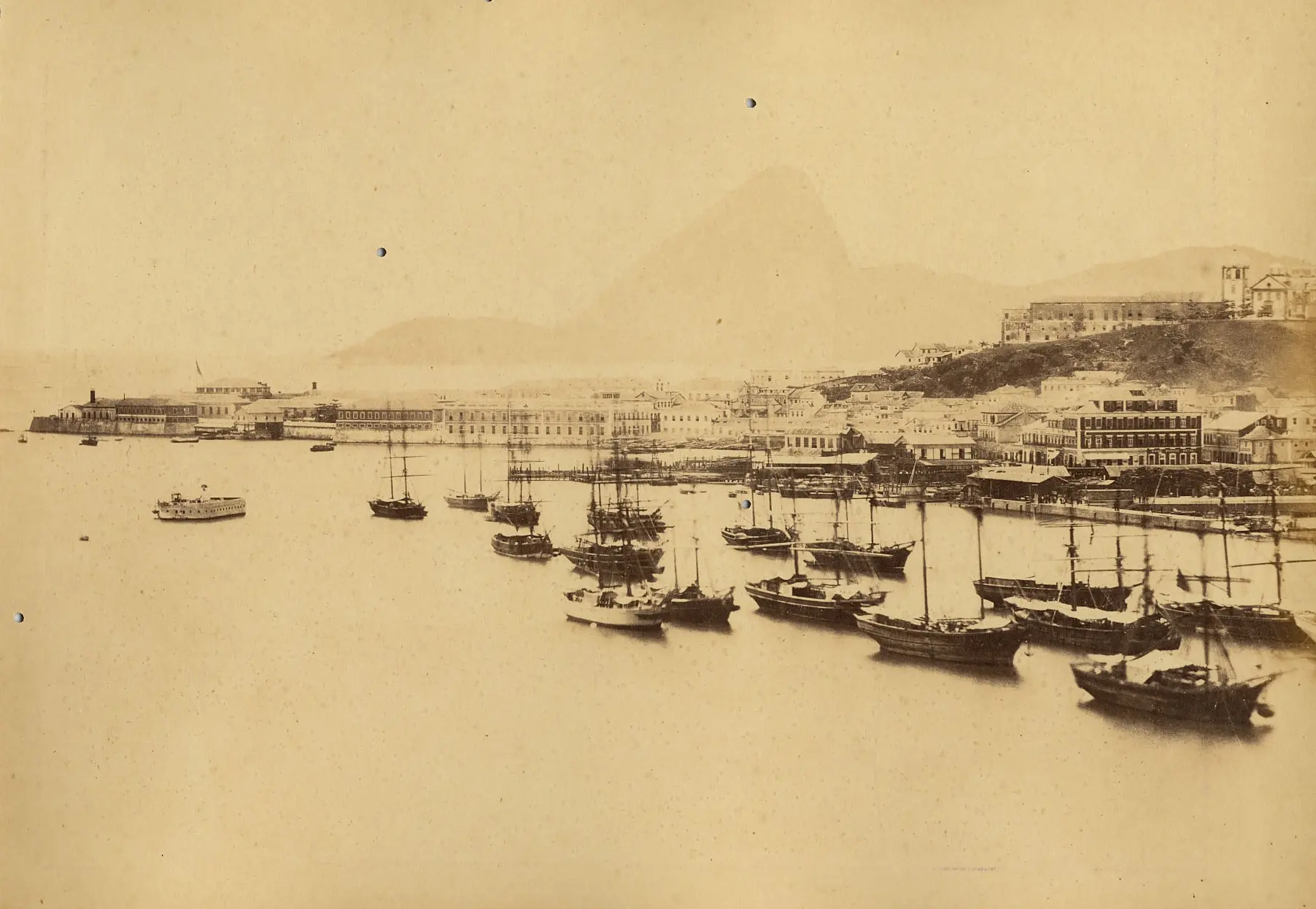 Porto antigo com navios e cidade ao fundo.
