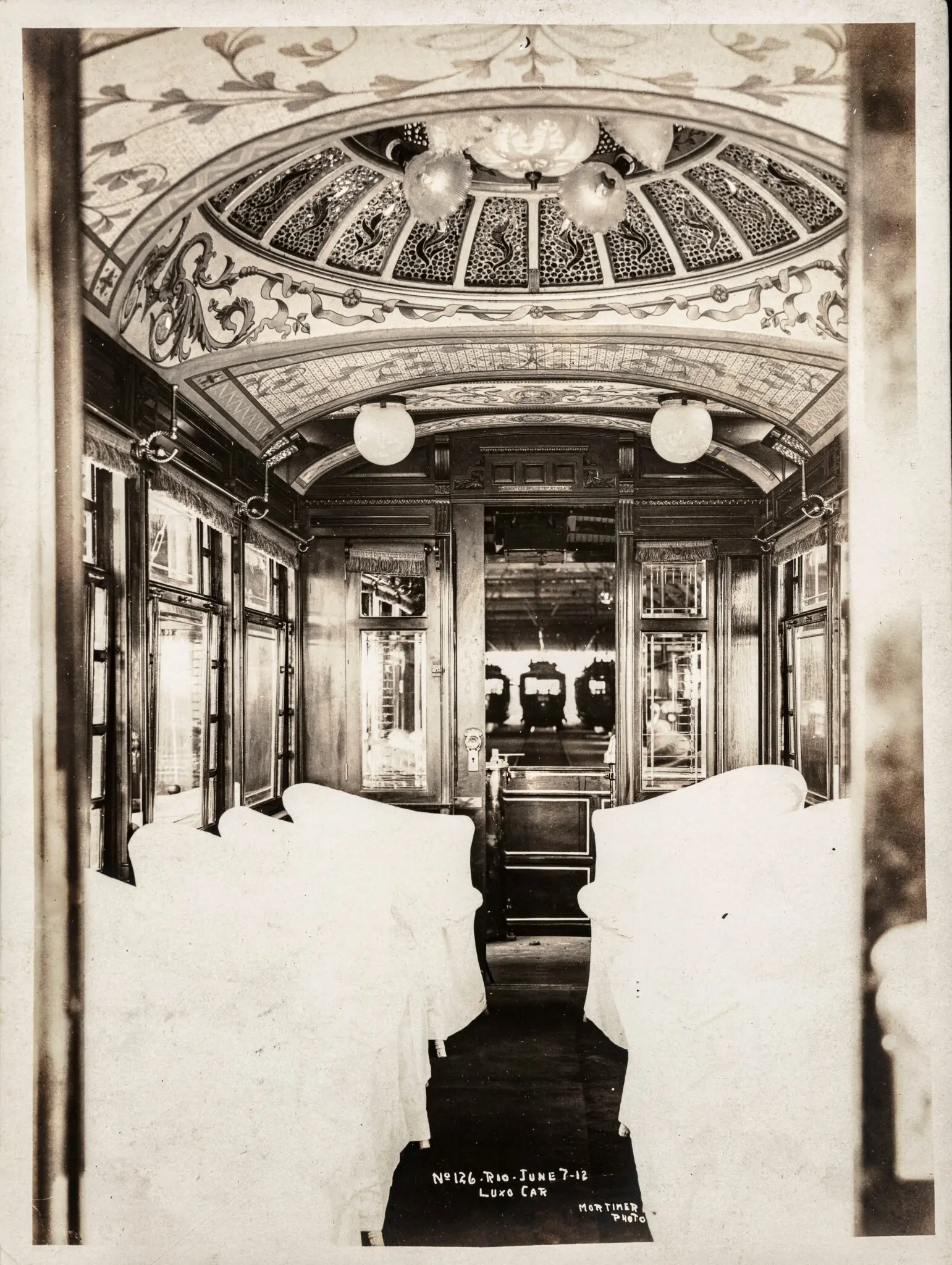 Interior de bondinho elétrico antigo, com assentos confortáveis e janelas grandes.