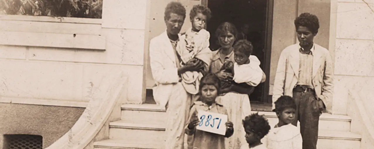 Família em frente à casa com escadas, preto e branco.