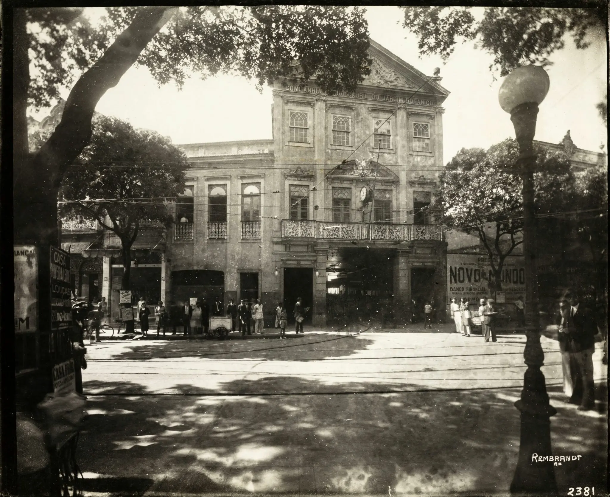 Edifício clássico com árvore grande e pessoas caminhando.
