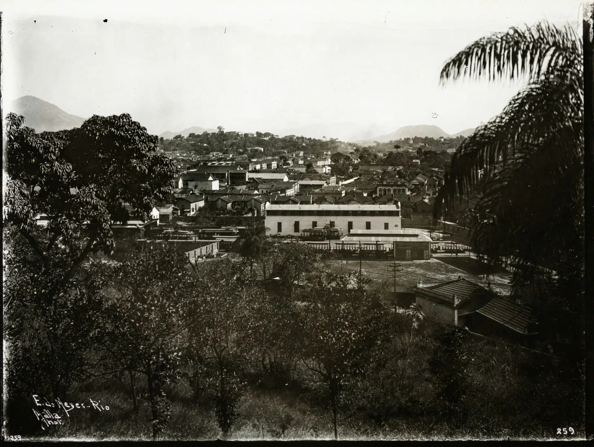 Paisagem urbana antiga em preto e branco, rodeada por montanhas e vegetação.