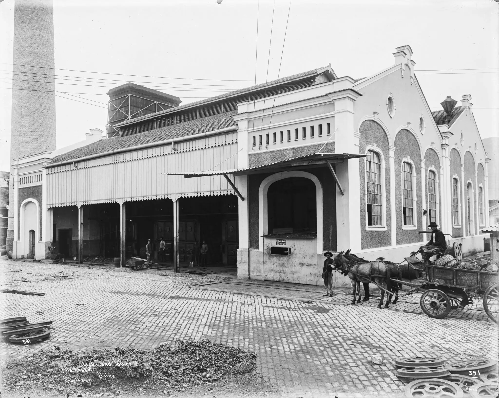 Edifício industrial histórico com carruagem e cavalos.