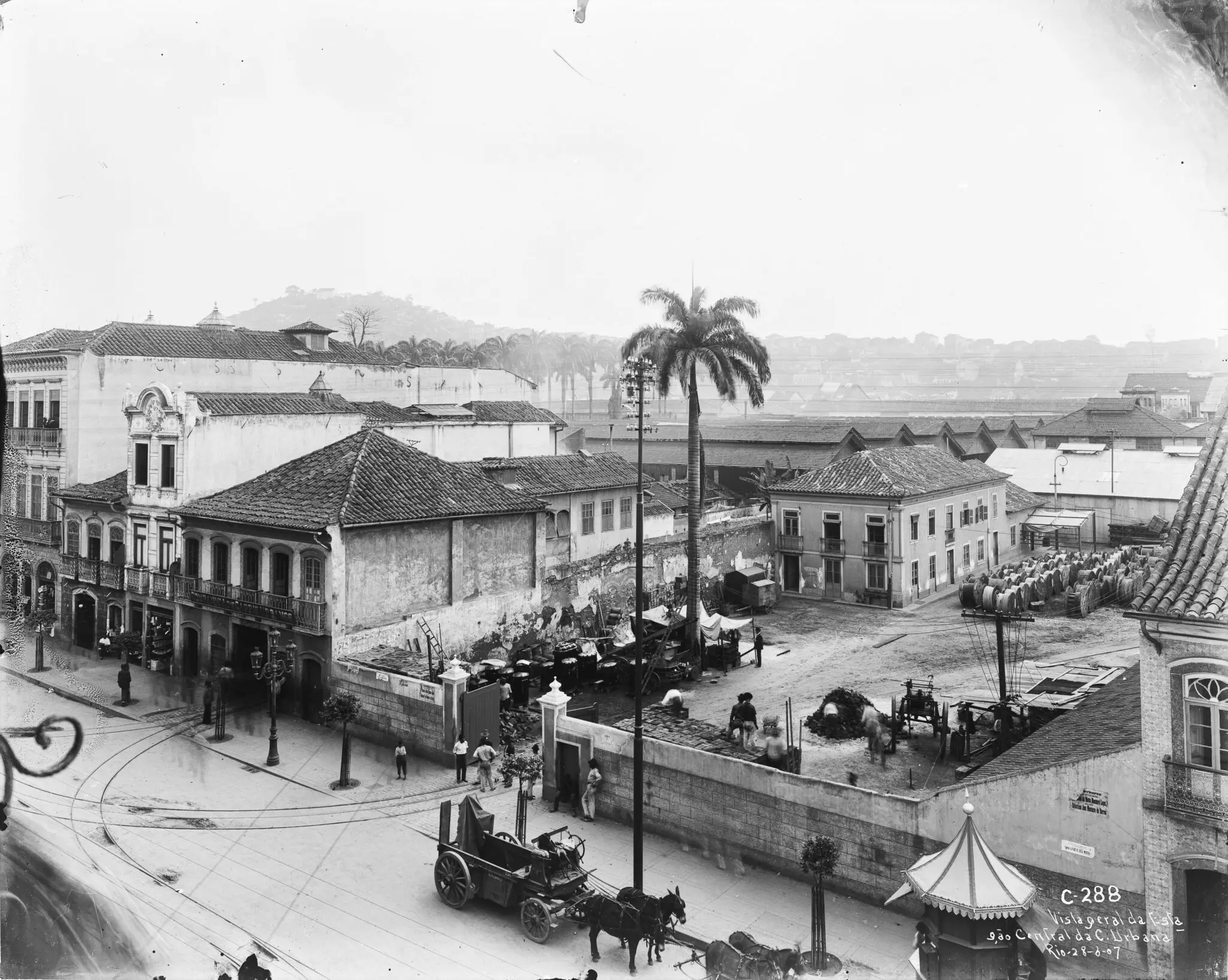 Praça urbana com palmeira, construções e feira.