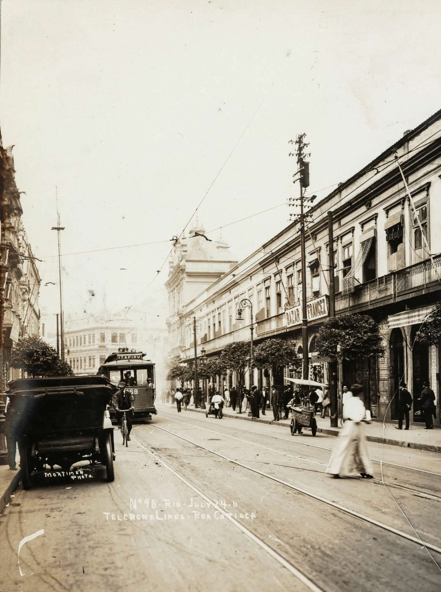 Uma rua urbana antiga com carruage, bicicleta e pessoas caminhando.