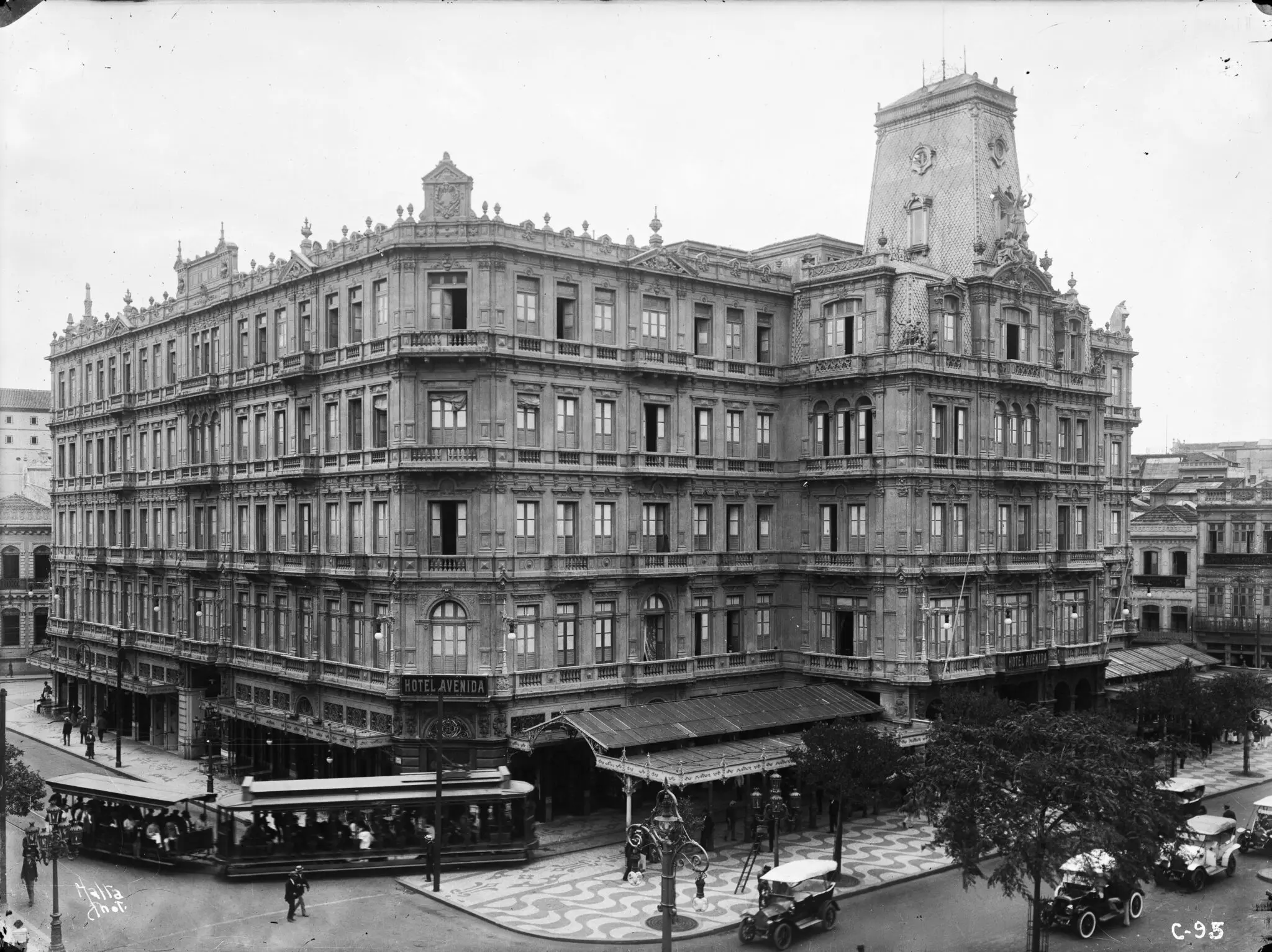 Edifício neoclássico com bonde e pessoas na rua.