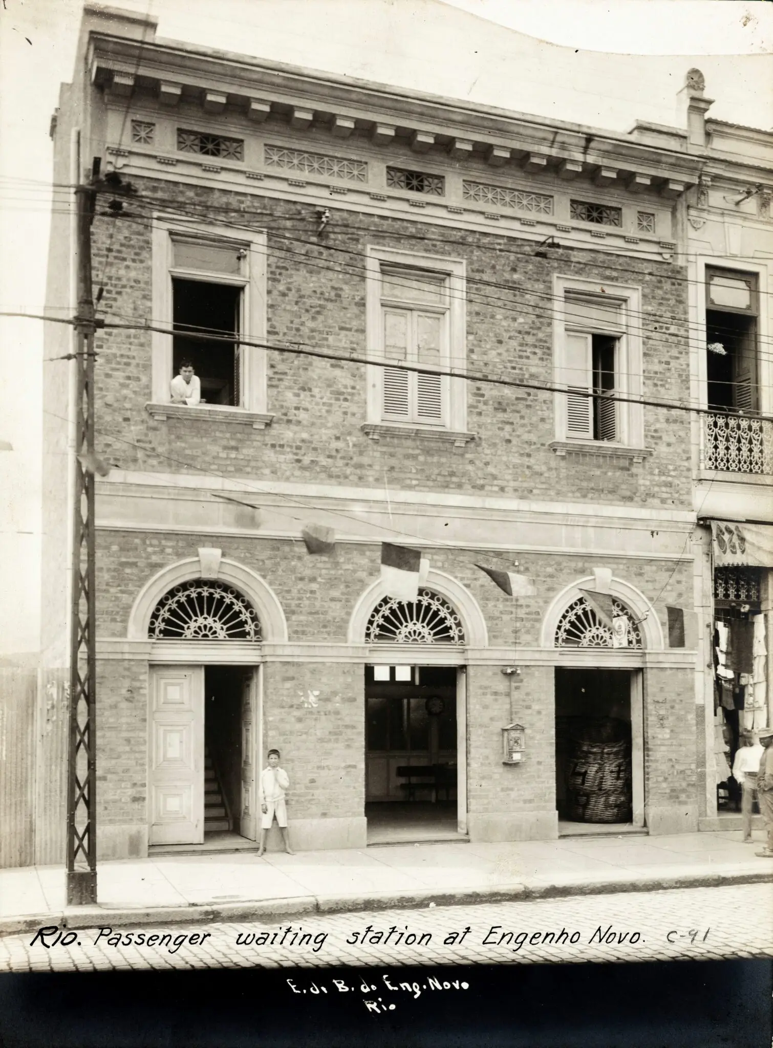 Edifício antigo com portas e janelas, pessoa à entrada, loja com objetos pendurados.