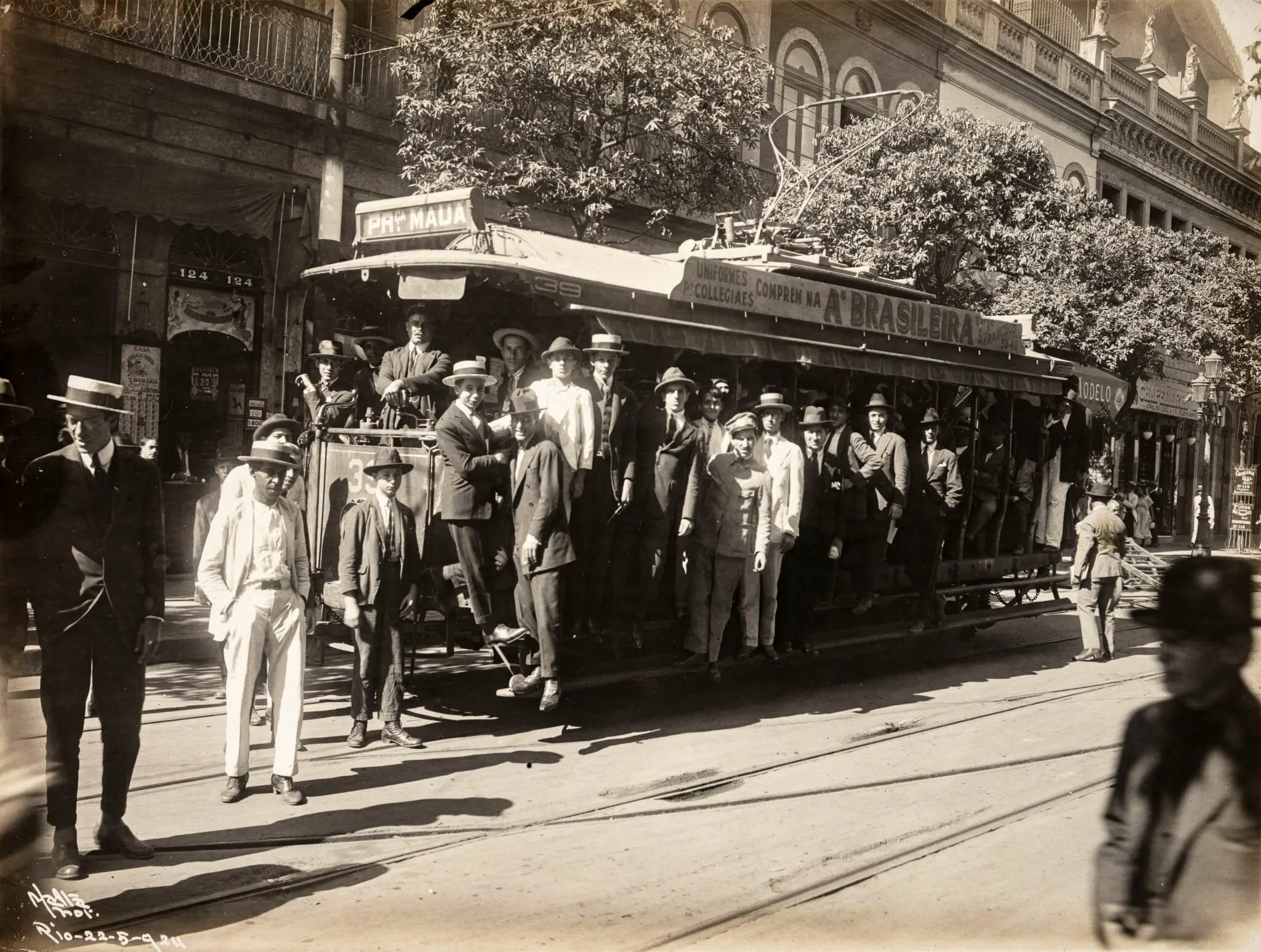 Grupo de pessoas em torno de um bonde em frente a edifício clássico.