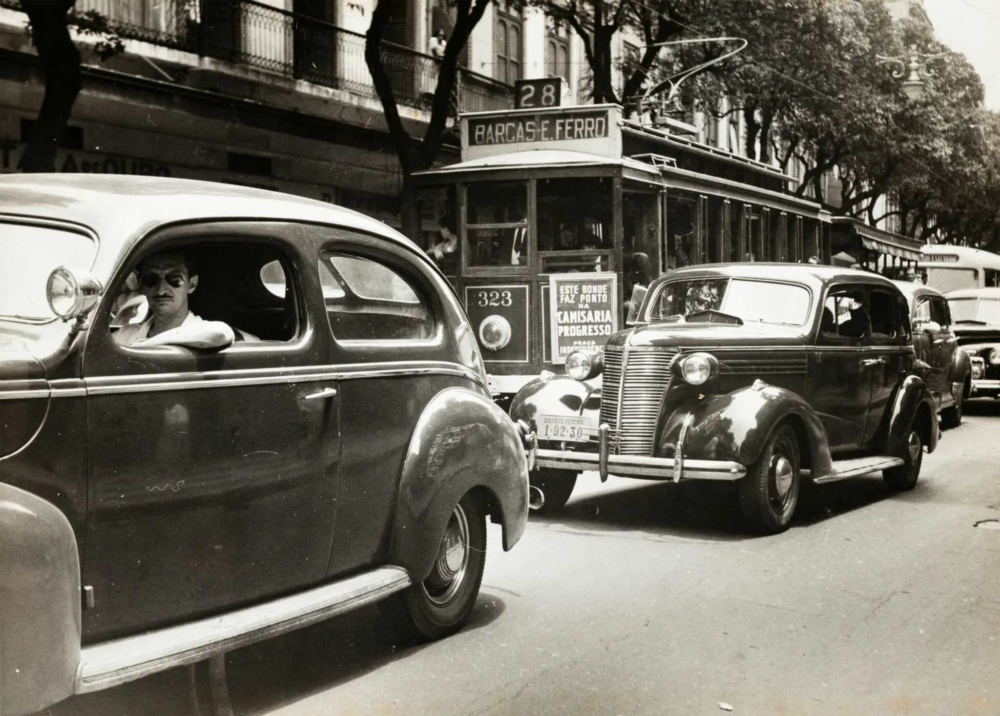 Cena urbana preto e branco com carro antigo e bonde.