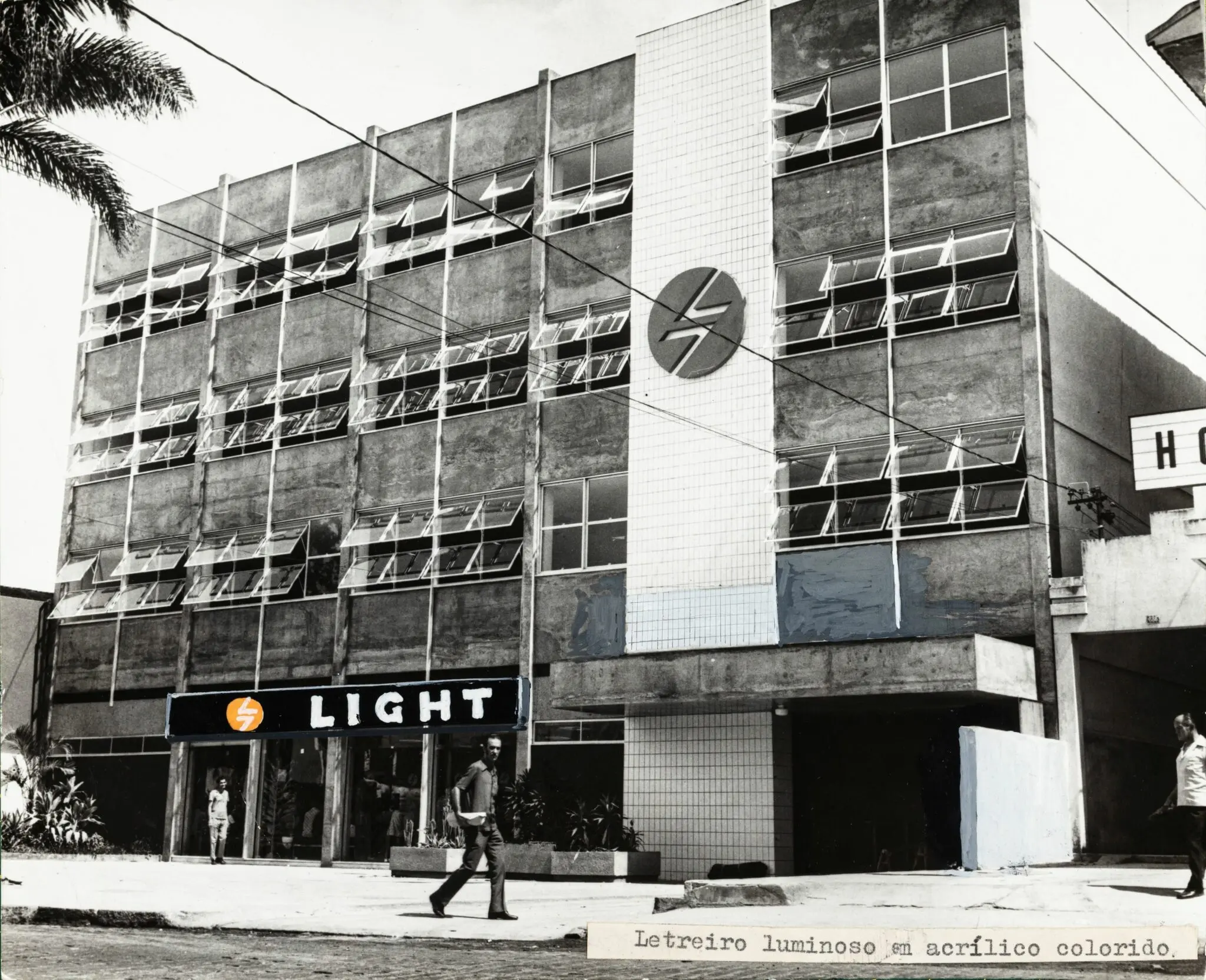 Fotografia preto e branco de prédio comercial com letreiro luminoso e estrutura metálica.
