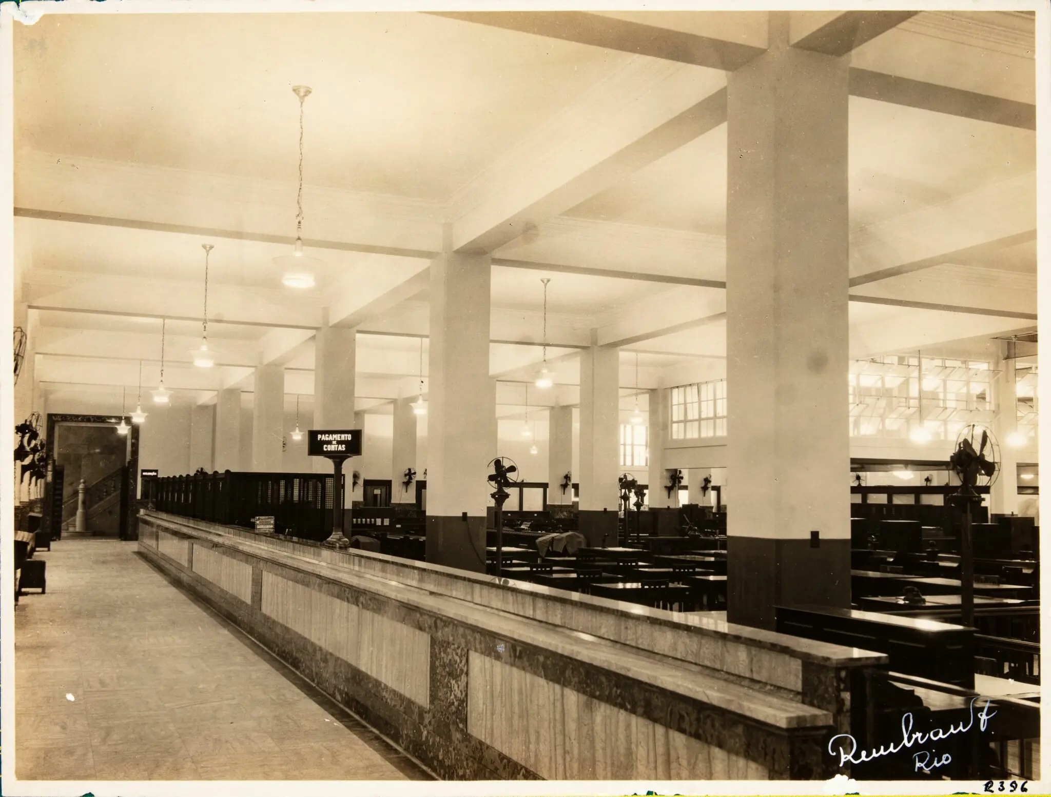Interior de agência bancária antiga em preto e branco.