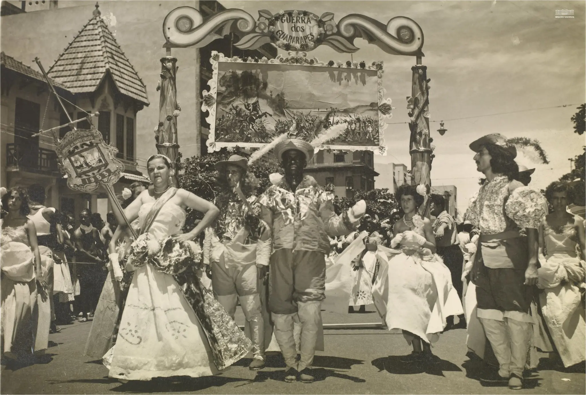 Fotografia preto e branco de parada festiva com dança e texto "GUERRA DOS GUARARAPES".